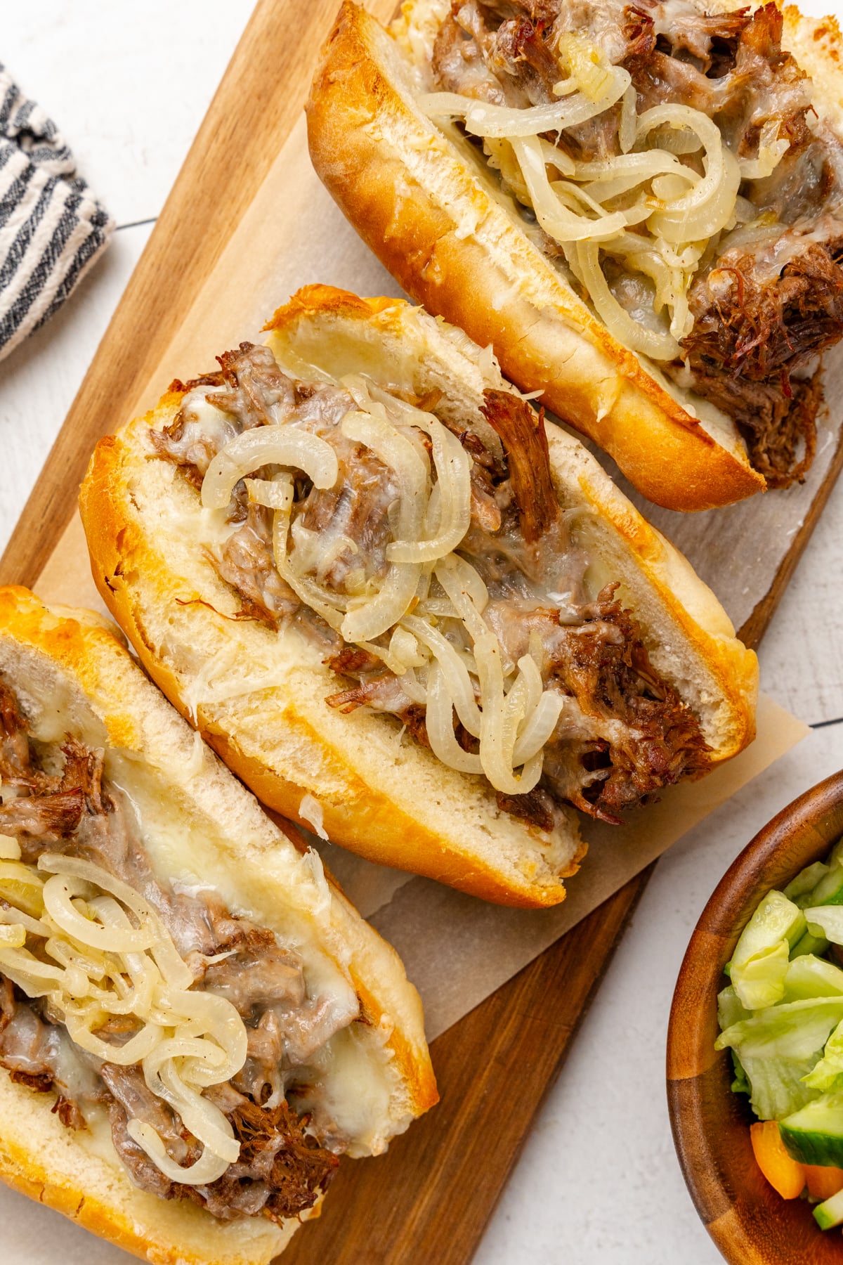 Roast beef sandwiches with melted cheese and sauteed onions in toasted buns are served with a side salad for a delicious weeknight meal, game day, or a get-together with friends.