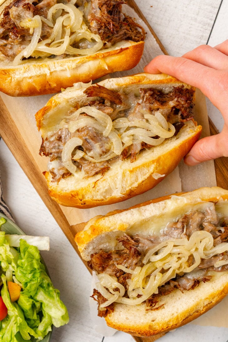 Roast beef sandwiches with melted cheese and sauteed onions in toasted buns are served with a side salad for a delicious weeknight meal, game day, or a get-together with friends.