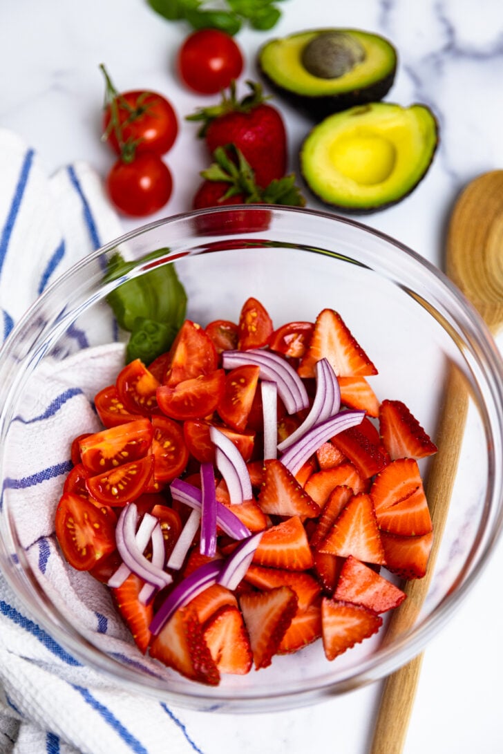Cut tomatoes, strawberries, red onion and avocado in a bowl to make a fresh delicious salad.