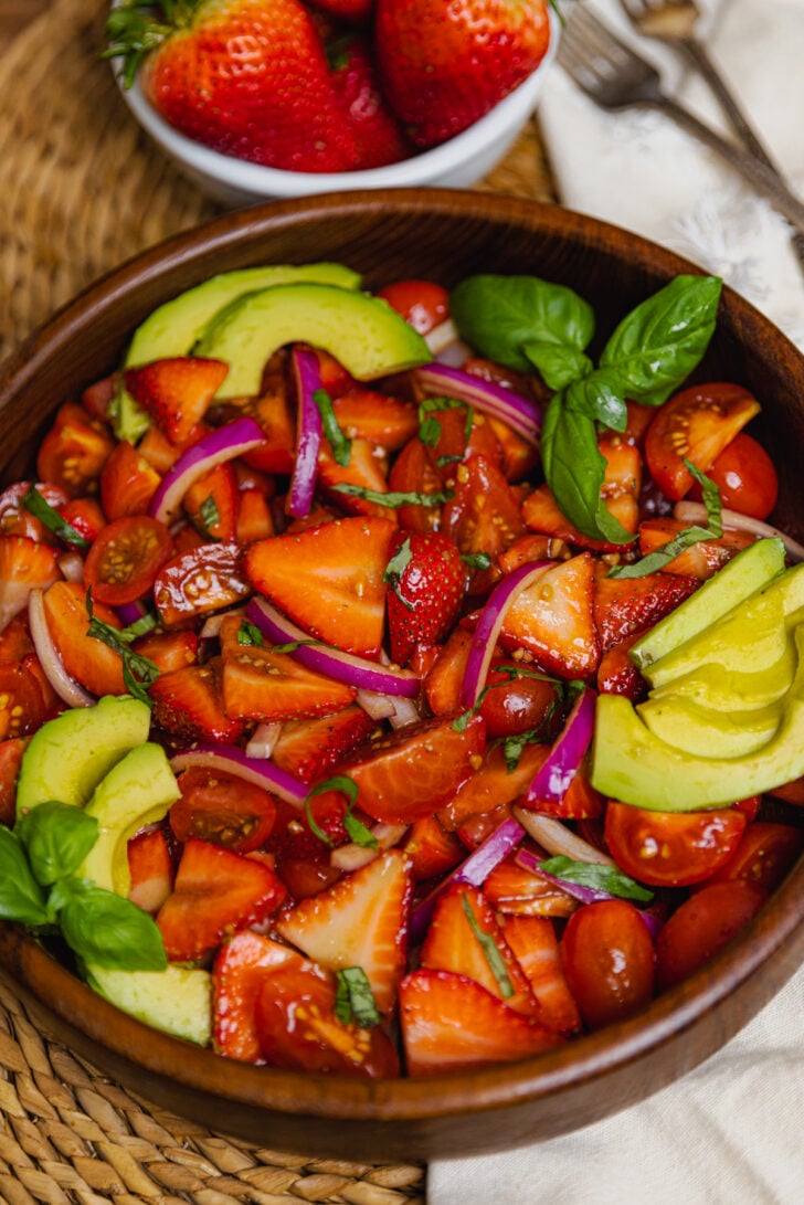 Wooden bowl with strawberry tomato avocado salad served with a silver spoon as a delicious side dish.
