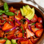 Wooden bowl with strawberry tomato avocado salad served with a silver spoon as a delicious side dish.