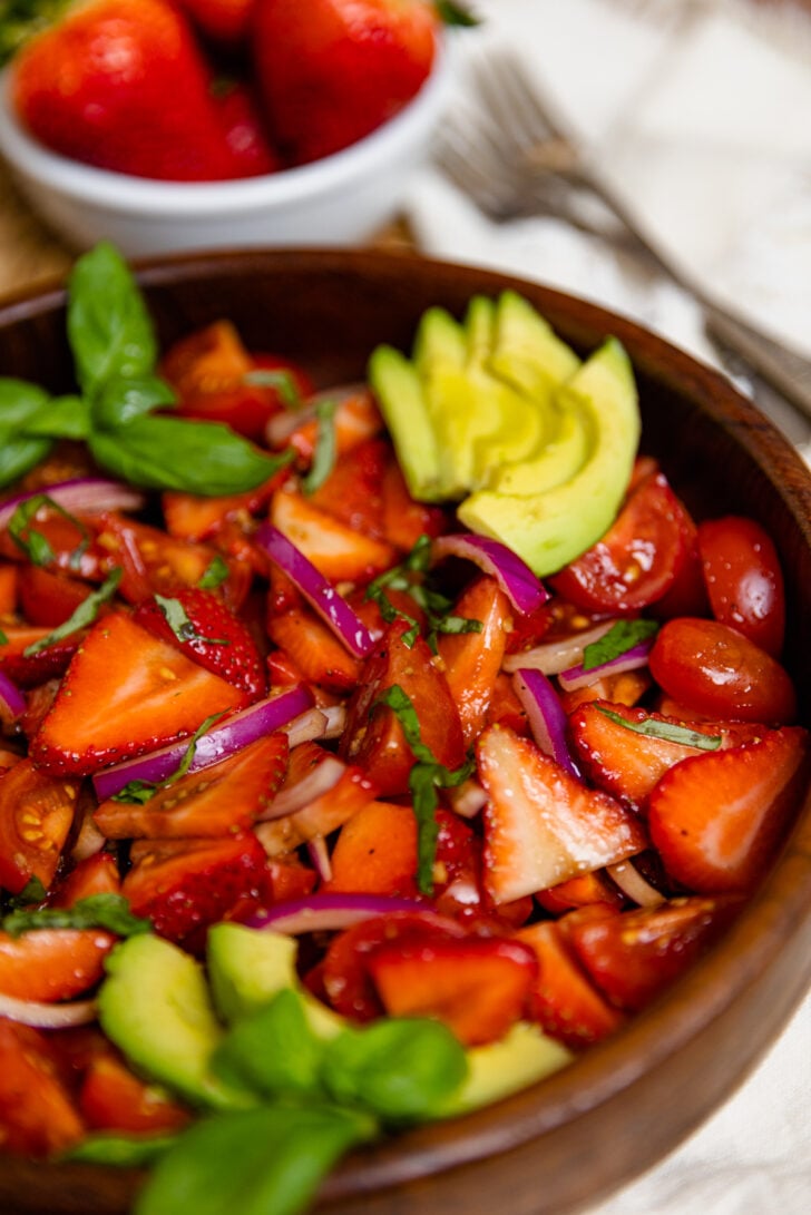 Wooden bowl with strawberry tomato avocado salad served with a silver spoon as a delicious side dish.