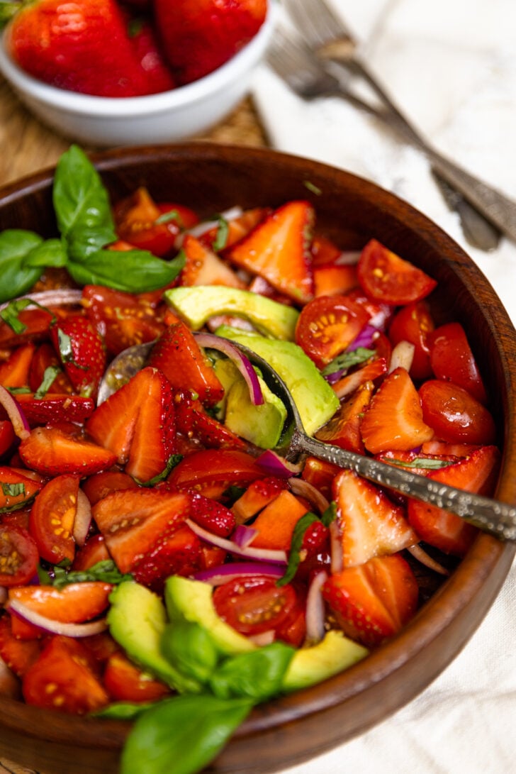 Wooden bowl with strawberry tomato avocado salad served with a silver spoon as a delicious side dish.