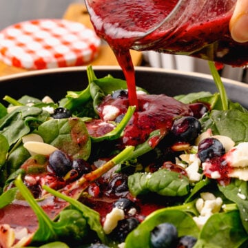 Jar of homemade blueberry vinaigrette salad dressing poured over fresh spinach, sliced almonds and feta cheese for a delicious, refreshing salad.