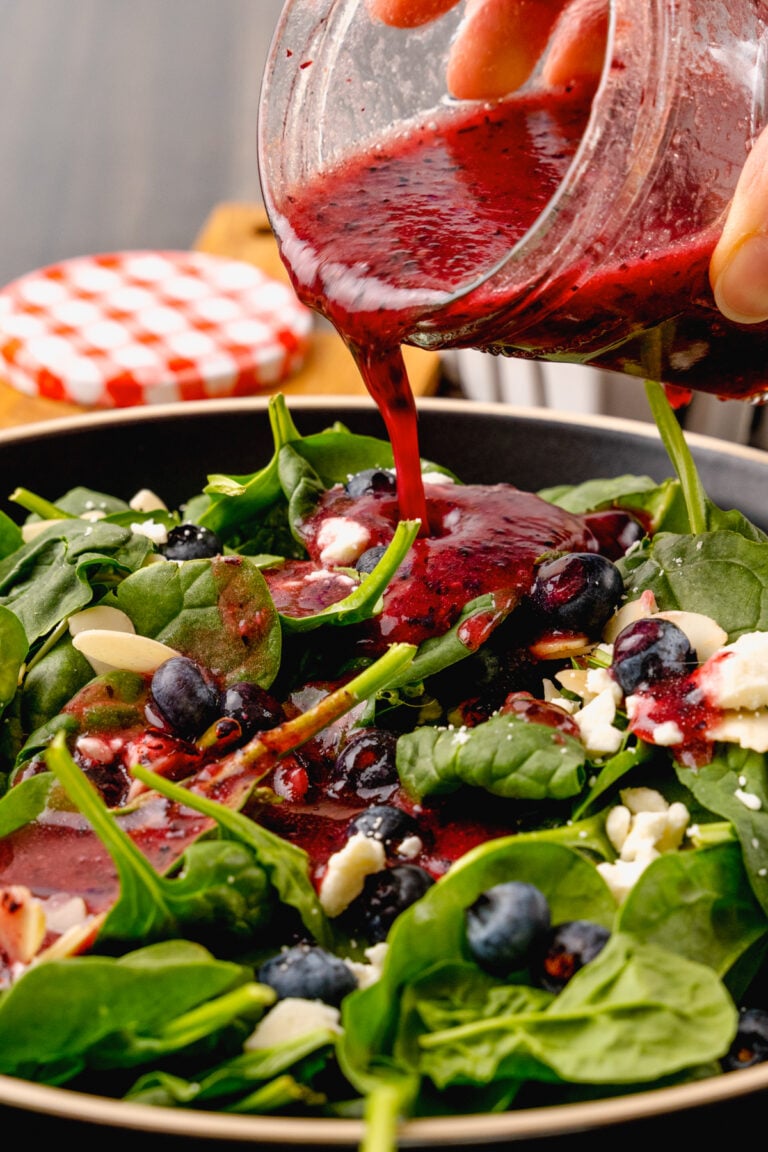 Jar of homemade blueberry vinaigrette salad dressing poured over fresh spinach, sliced almonds and feta cheese for a delicious, refreshing salad.