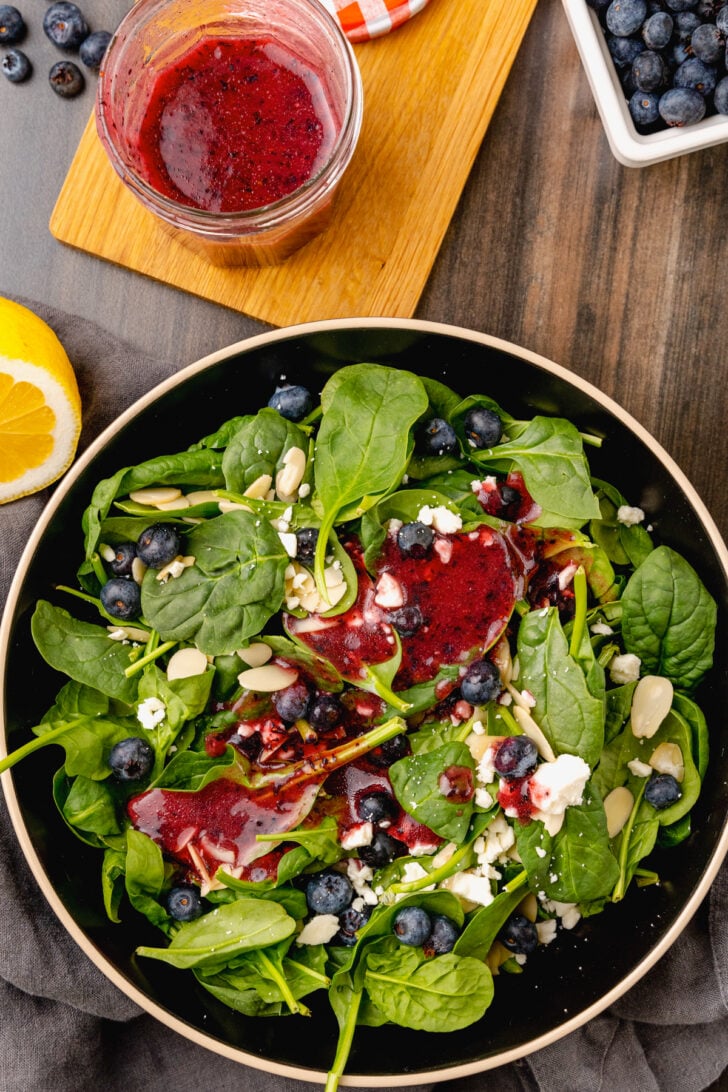 Bowl of salad greens with blueberries, almonds and feta cheese drizzled with homemade blueberry vinaigrette salad dressing.