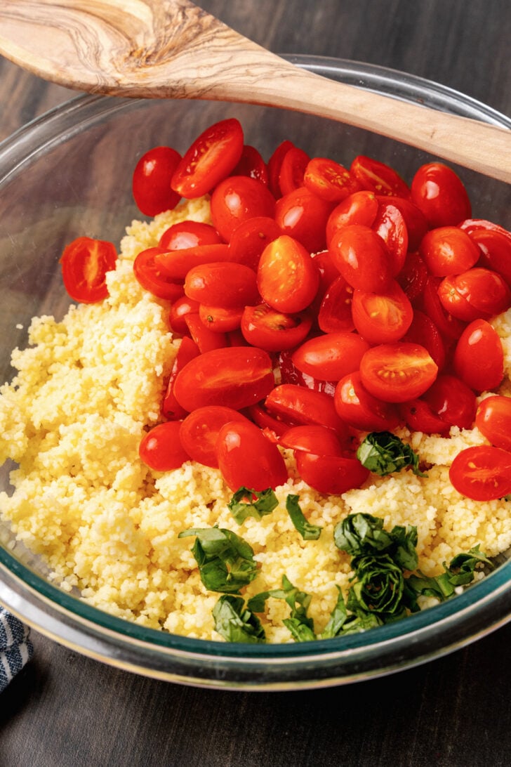 Perfectly cooked couscous, sliced grape tomatoes, and fresh tomatoes in a glass bowl to be tossed in a bright dressing for a delicious salad.