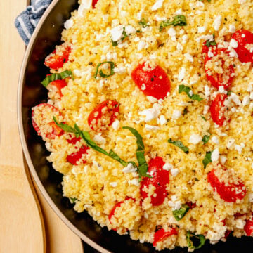 Big bowl of couscous salad with feta, tomatoes and fresh basil served as a side dish for lunch, dinner or at a picnic, cookout or family gathering.