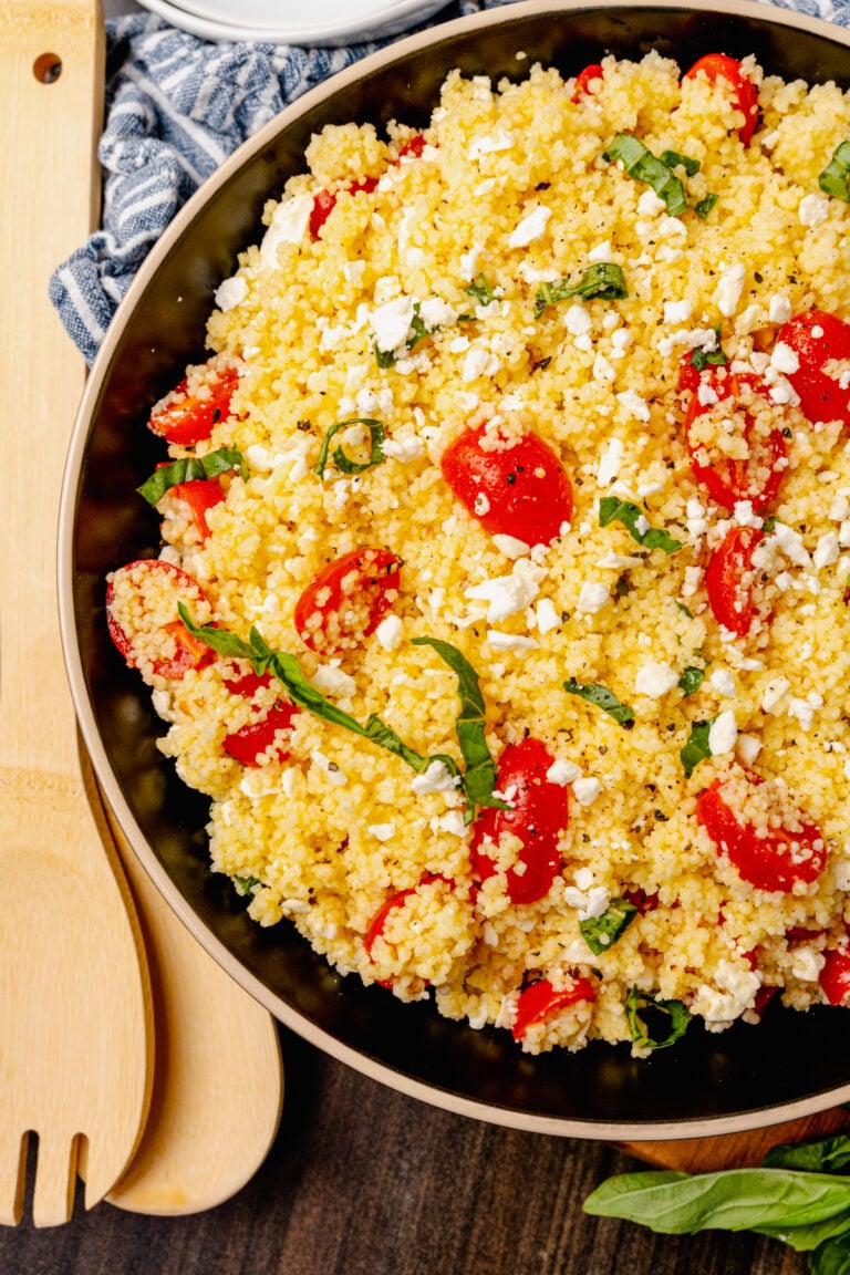 Big bowl of couscous salad with feta, tomatoes and fresh basil served as a side dish for lunch, dinner or at a picnic, cookout or family gathering.