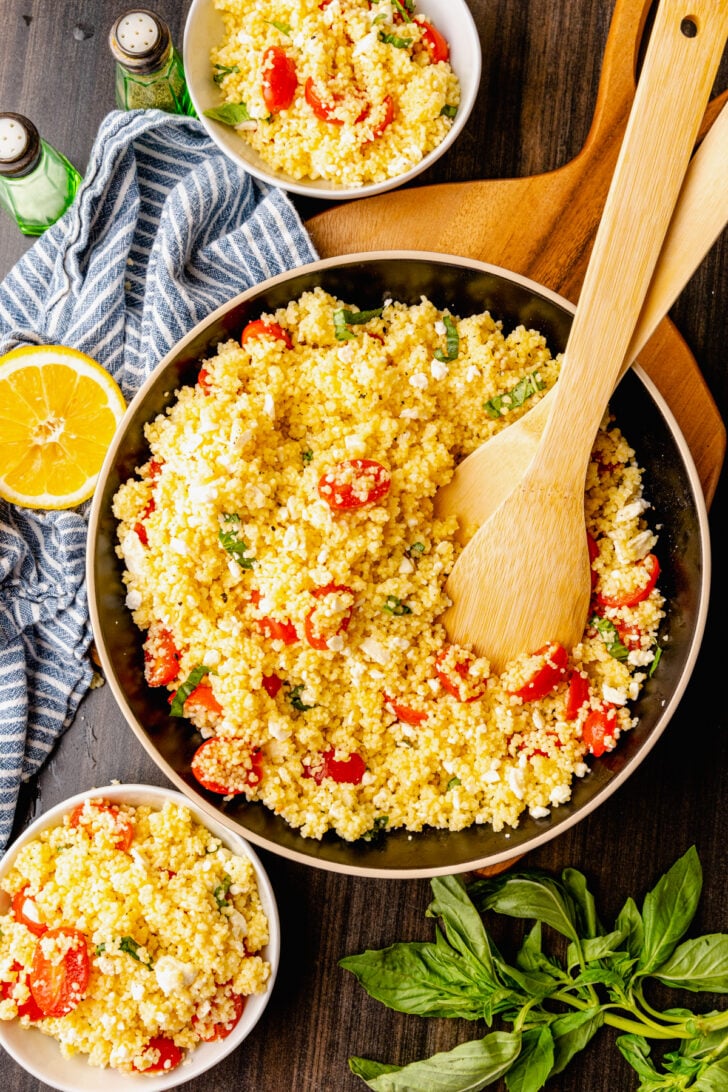 Big bowl of couscous salad with feta, tomatoes and fresh basil served as a side dish for lunch, dinner or at a picnic, cookout or family gathering.