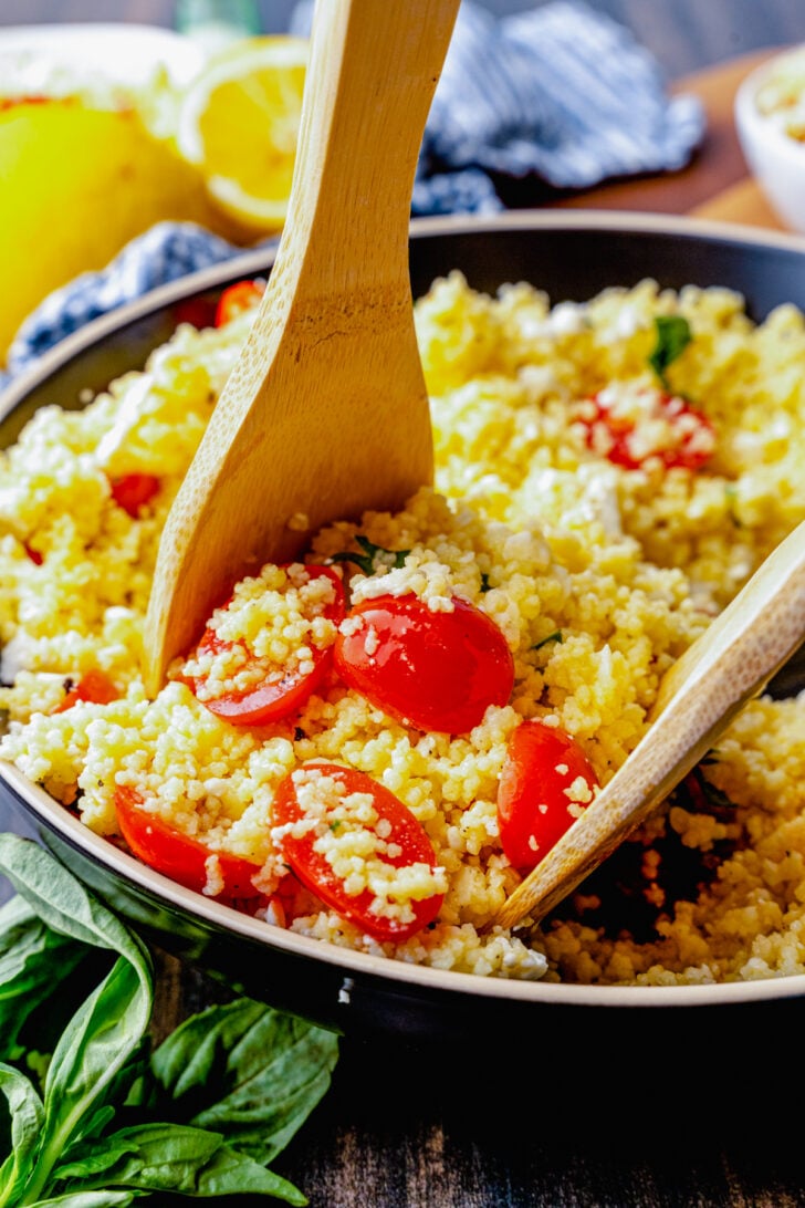 Big bowl of couscous salad with feta, tomatoes and fresh basil served as a side dish for lunch, dinner or at a picnic, cookout or family gathering.