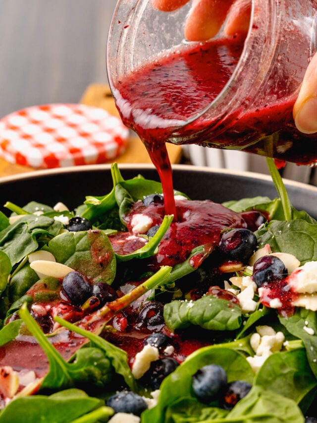 Jar of homemade blueberry vinaigrette salad dressing poured over fresh spinach, sliced almonds and feta cheese for a delicious, refreshing salad.