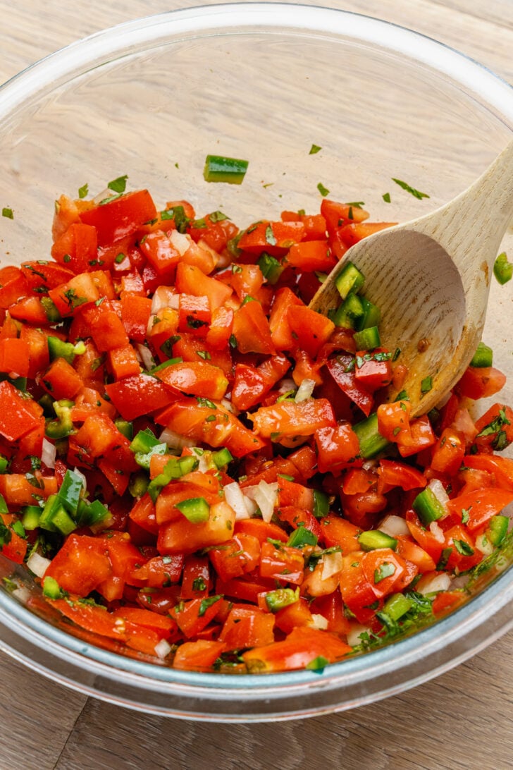 Glass mixing bowl with chopped tomatoes, jalapenos, onions, cilantro and lime juice to make fresh pico de gallo.