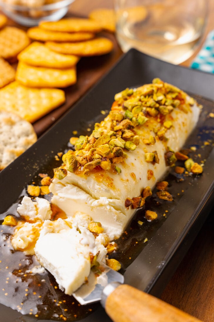Goat cheese log with fig jam, honey and sprinked with chopped pistachios served on a black platter for cocktails.