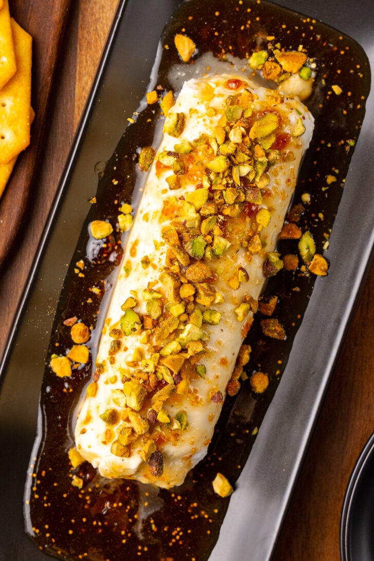 Goat cheese log with fig jxaam, honey and sprinked with chopped pistachios served on a black platter and a knife for cocktails.