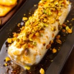 Goat cheese log with fig jxaam, honey and sprinked with chopped pistachios served on a black platter for cocktails.