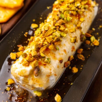 Goat cheese log with fig jxaam, honey and sprinked with chopped pistachios served on a black platter for cocktails.