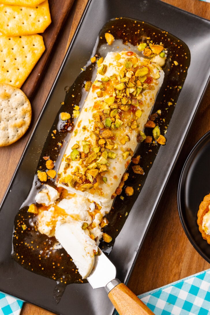 Goat cheese log with fig jxaam, honey and sprinked with chopped pistachios served on a black platter and a knife for cocktails.