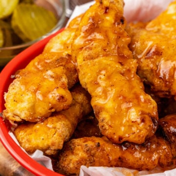 Red basket with Nashville Hot Chicken Tenders cooked in the air fyer area crispy and spicy served with pickles.