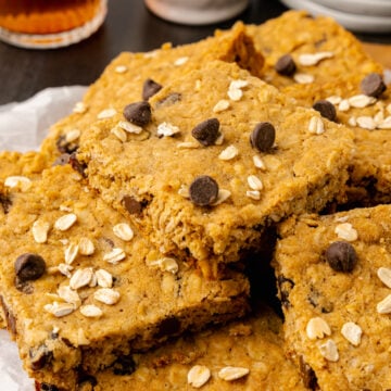 Oatmeal chocolate chip cookie bars stacked on a white plate served along side cup of tea.