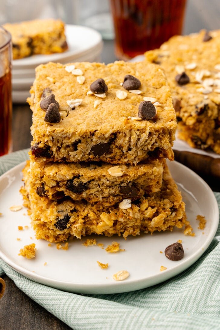 Oatmeal chocolate chip cookie bars stacked on a white plate served along side cup of tea.
