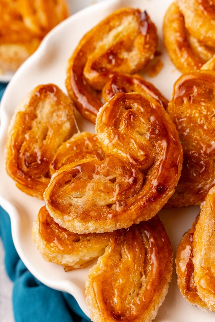 Classic Palmiers with a dashed of cinnamon baked until golden brown served on a white cake stand with a blue napkin.