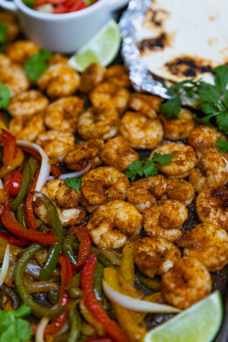 Chilli lime shrimp with peppers and onions cooked on a sheet pan served with tortillas and fresh cilantro make a delicious meal of Chili Lime Shrimp Fajitas.