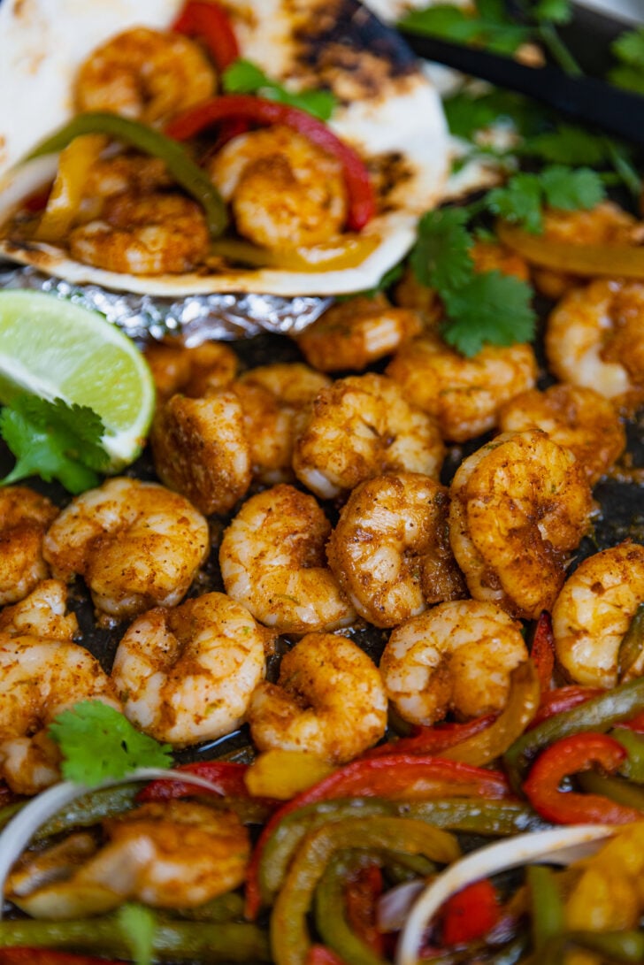 Chilli lime shrimp with peppers and onions cooked on a sheet pan served with tortillas and fresh cilantro make a delicious meal of Chili Lime Shrimp Fajitas.
