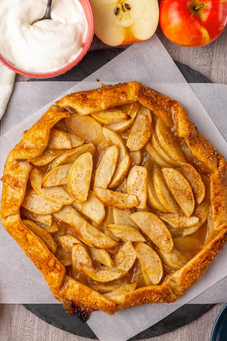 Golden and beautifully baked Apple Crostata served with homemade whipped cream, being cooled on parchment paper.