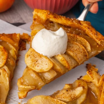 Sliced Apple Crostata sliced and being served with a pie server and homemade whipped cream.
