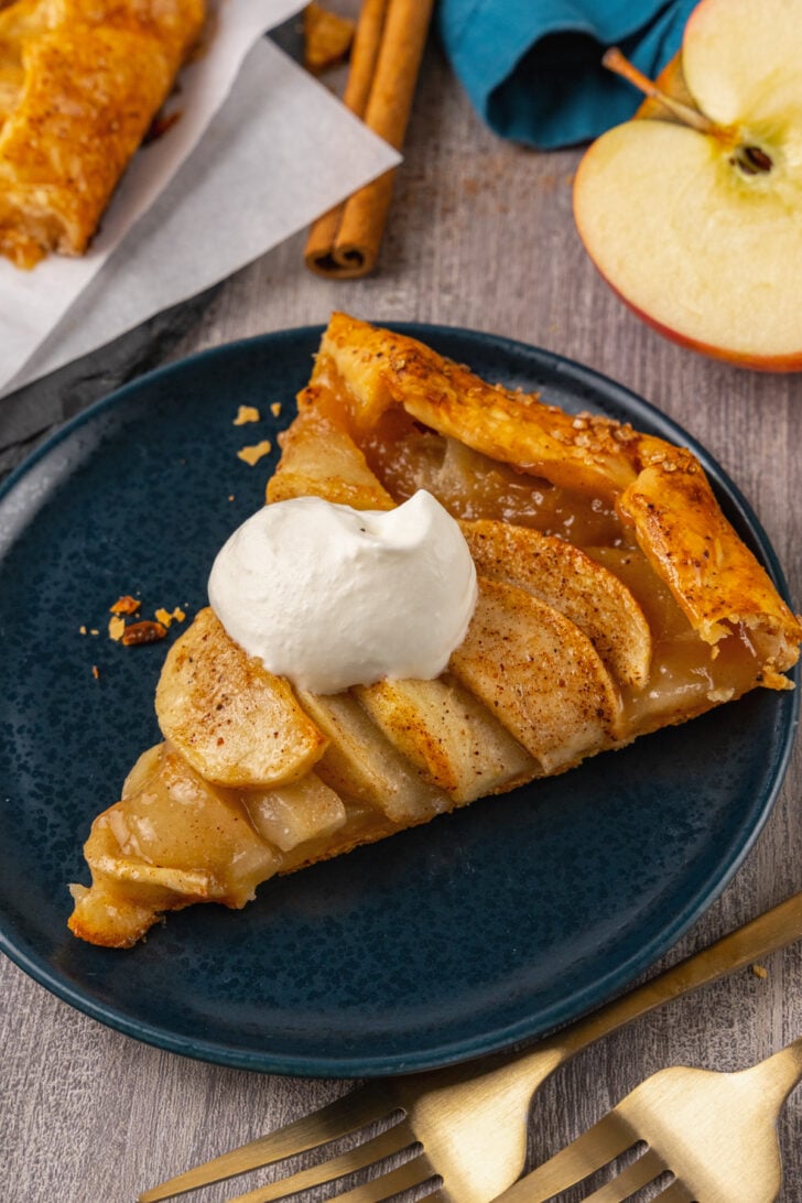 Golden and beautifully baked Apple Crostata served with homemade whipped cream, served on a place with a gold fork.