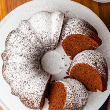 Southern chocolate pound cake dusted with powdered cake with 3 slices on a white cake is amazingly delicious.