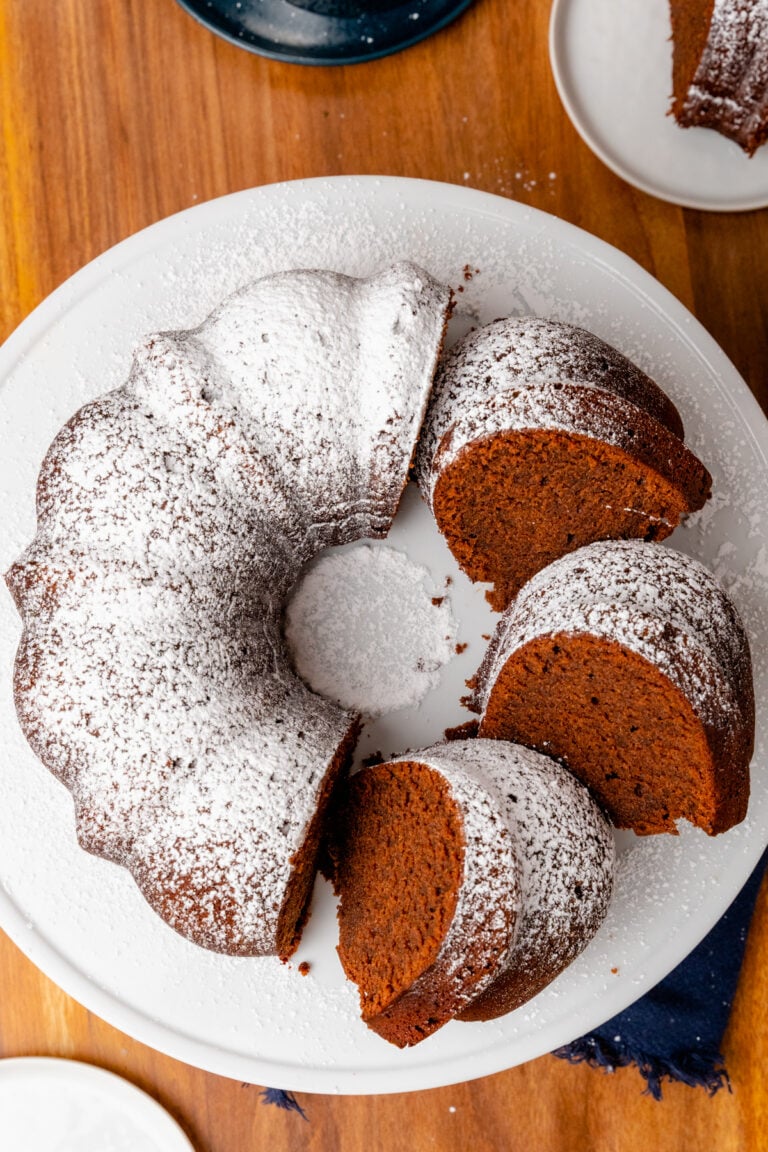 Southern chocolate pound cake dusted with powdered cake with 3 slices on a white cake is amazingly delicious.