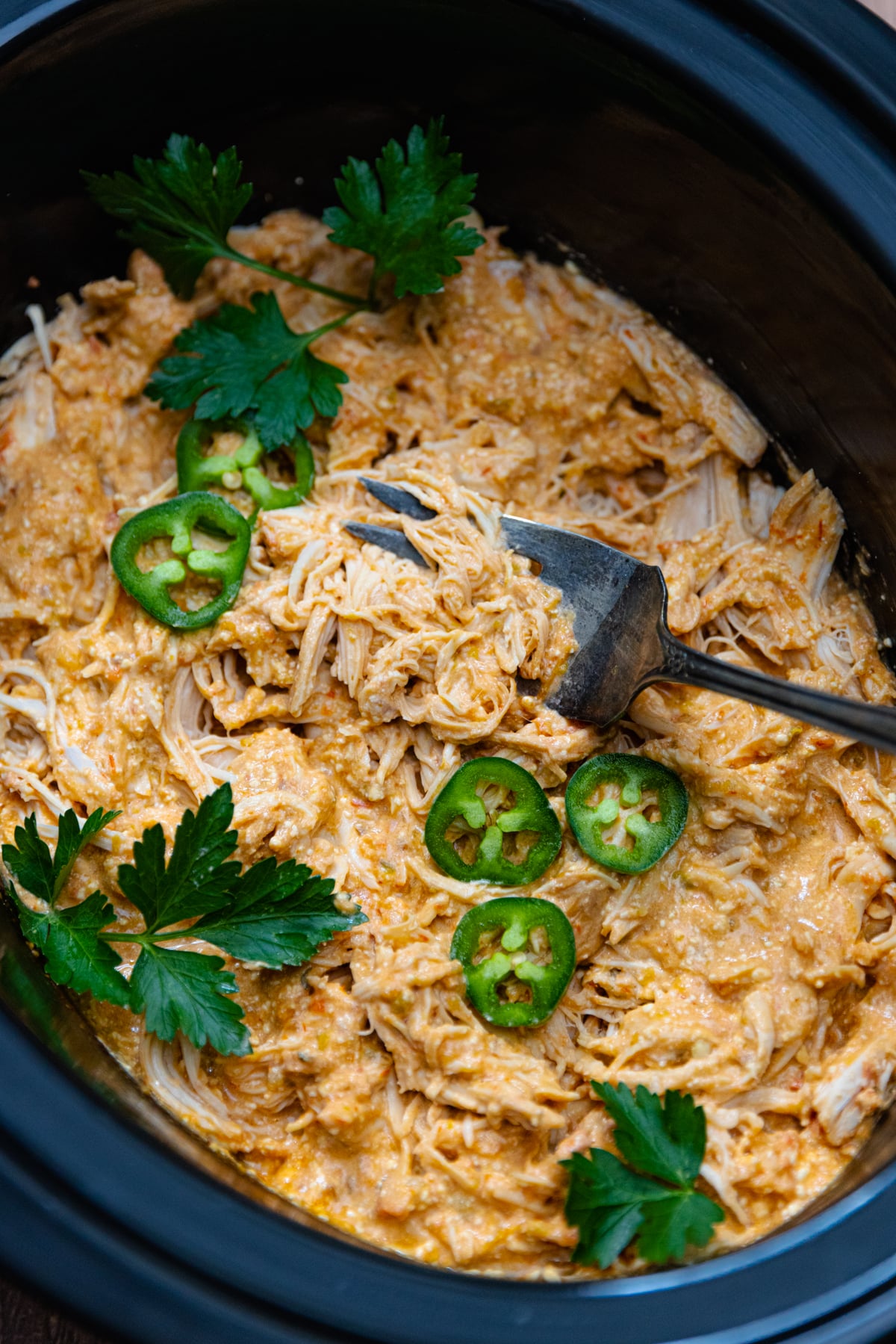 Crock Pot cooked chicken breasts cooked in salsa, cream cheese and seasoning the shredded and served with sliced jalapenose and fresh parsley.