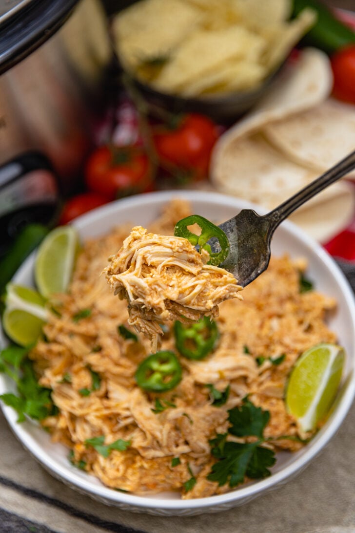 White bowl of shredded cream cheese salsa chicken cooked in the crock pot topped with jalapenos, fresh parsley and lime wedges.