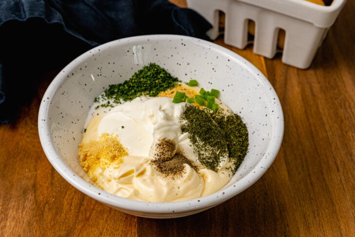 White bowl with mayonnaise, sour cream, chives, pepper, dill, garlic and onion powder for ranch dressing.