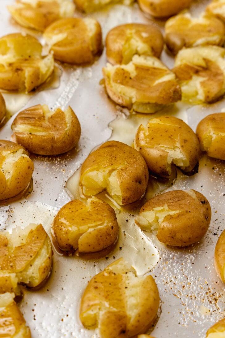Baking sheet lines with foil with baby potatoes cooked in olive oil, salt and pepper then smashed with a fork.