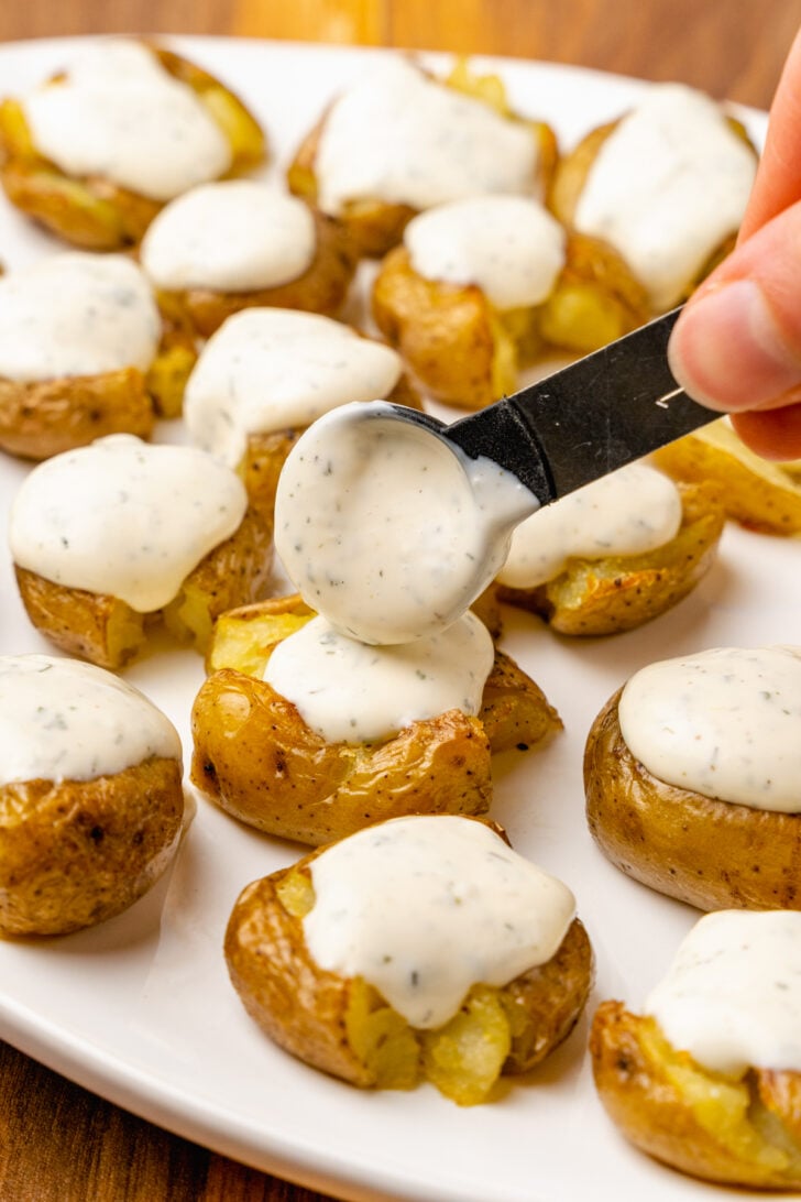 Crushed baby potatoes roasted until crispy and golden served on a white platter and topped with homemade ranch dressing.