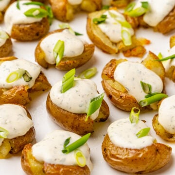 Crushed baby potatoes topped with homemade ranch dressing and chopped green onions served on a white platter