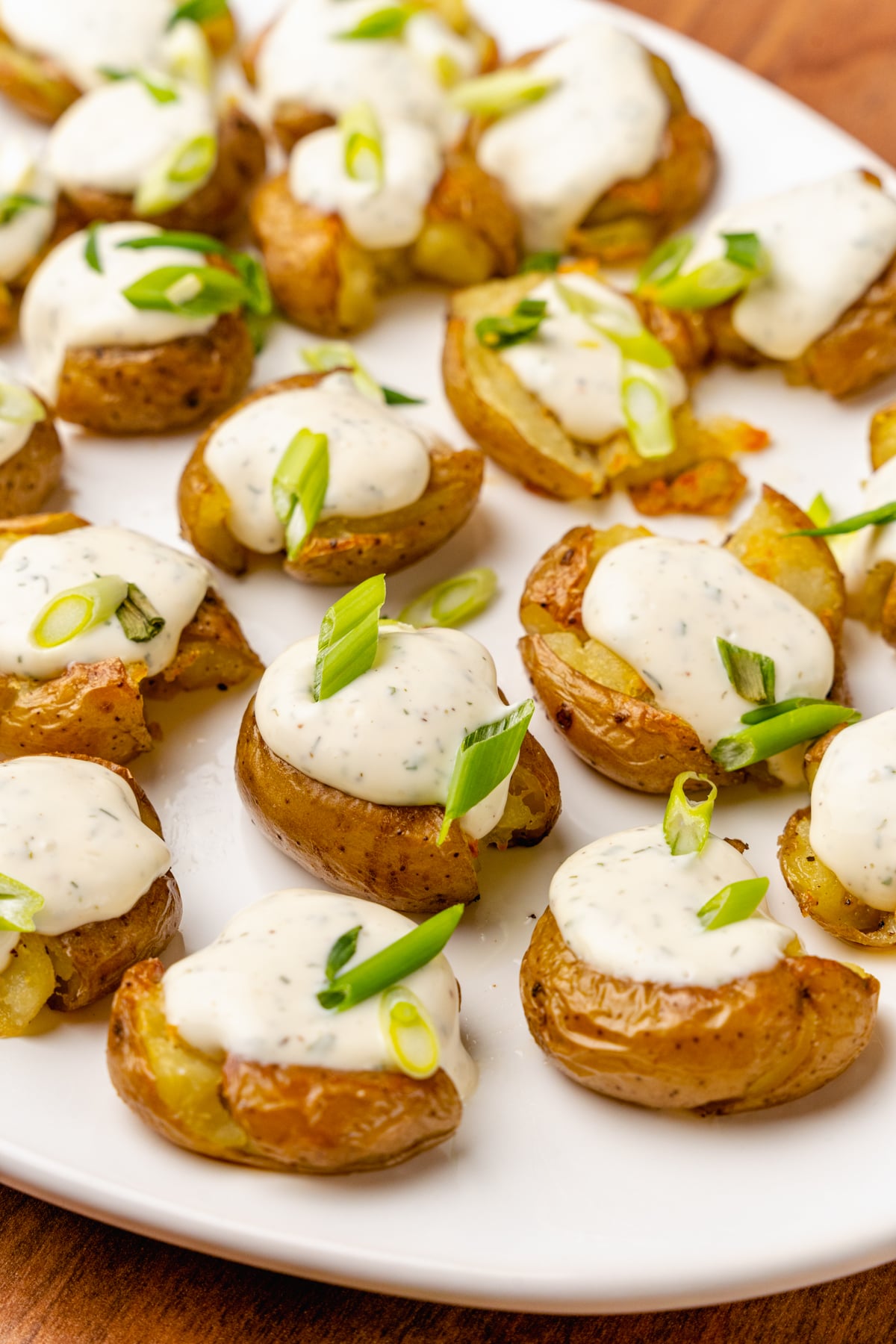 Crushed baby potatoes topped with homemade ranch dressing and chopped green onions served on a white platter