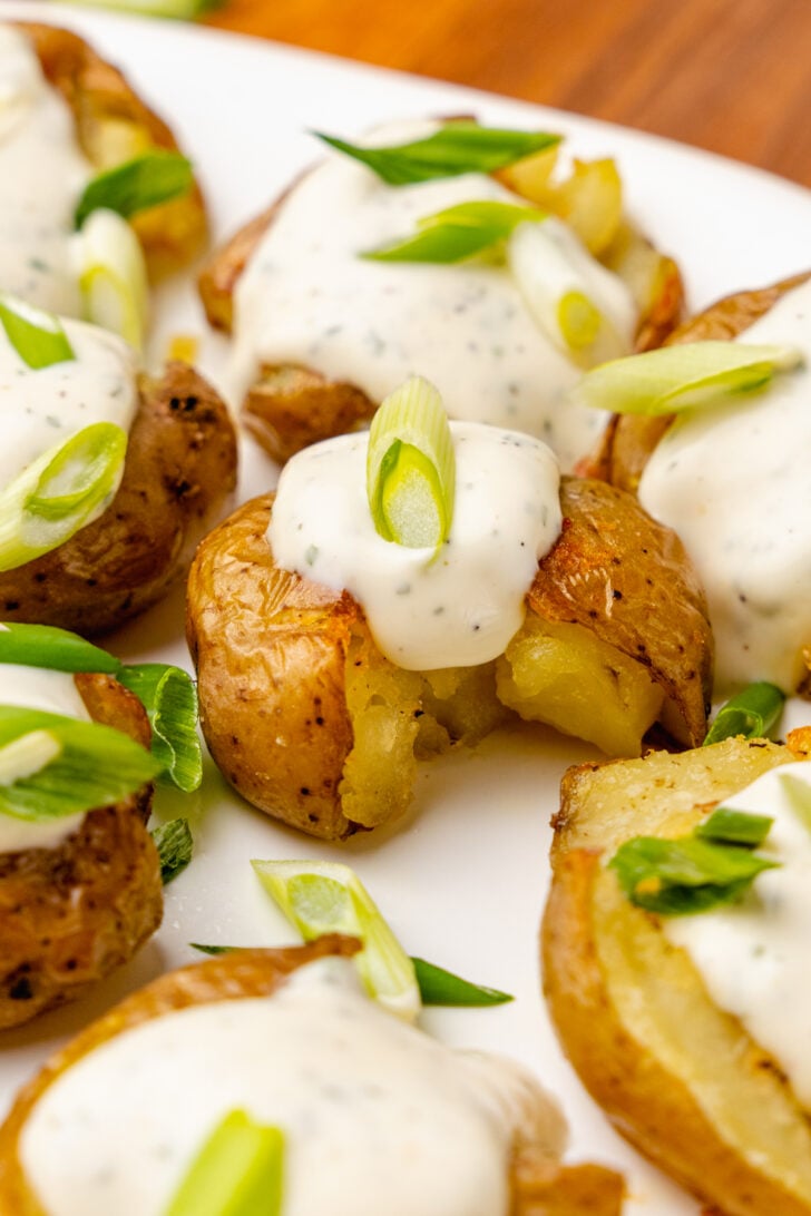 Crushed baby potatoes topped with homemade ranch dressing and chopped green onions served on a white platter.