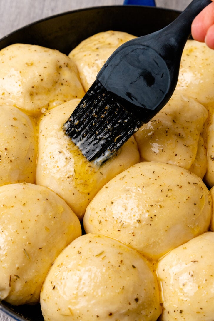 Unbaked dinner rolls brushed with melted butter, herbs, garlic and Parmesan cheese to be baked in a cast iron skillet.