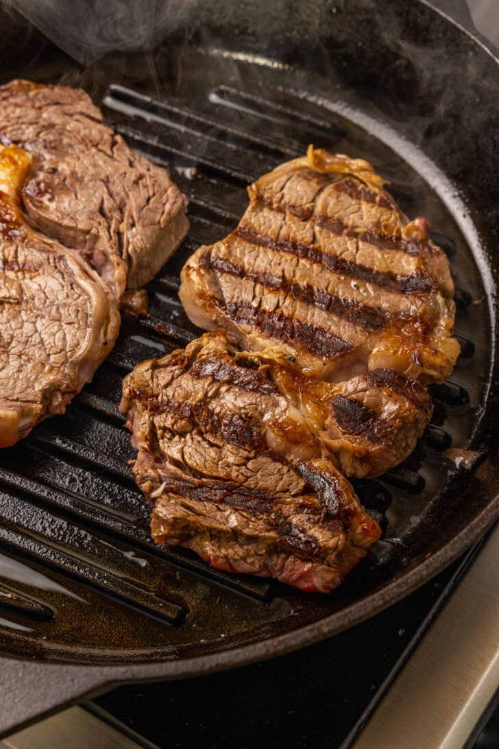 Ribeye steaks on a grilled pan, seasoned with salt and pepper cooked perfectly for steak salad.