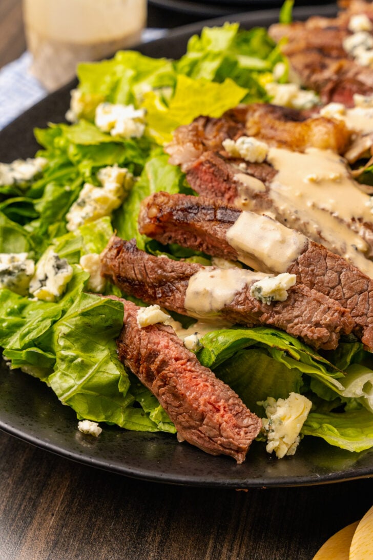 Grilled Steak Salad with blue cheese, creamy vinaigrette salad dressing and chopped romaine lettuce with blue cheese crumbles served on a black platter.