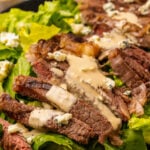 Grilled Steak Salad with blue cheese, creamy vinaigrette salad dressing and chopped romaine lettuce with blue cheese crumbles served on a black platter.