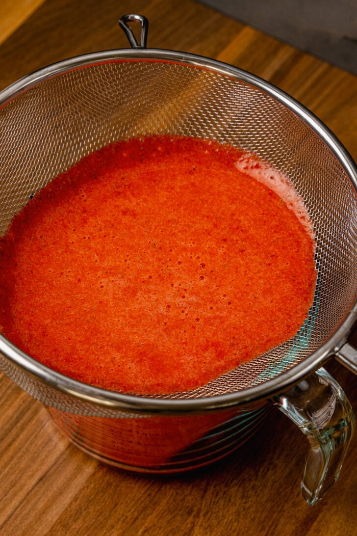 Fresh strawberry puree being strained into a glass measuring cup to be used in margaritas.