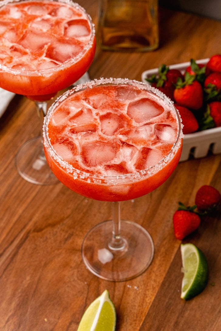 Sugar, salt rimmed glass rimmed glass with a fresh strawberry margarita with ice made with fresh fruit and limes.