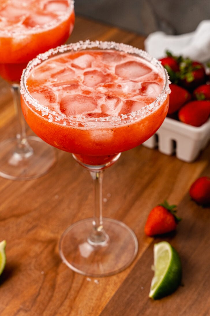 Sugar, salt rimmed glass rimmed glass with a fresh strawberry margarita with ice made with fresh fruit and limes.