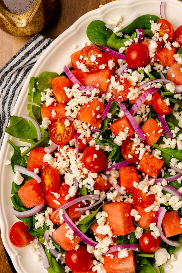 White serving platter loaded with fresh watermelon, grape tomatoes, red onion, spinach and feta cheese is an easy to make side dish for any spring or summer gathering.