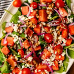 White serving platter loaded with fresh watermelon, grape tomatoes, red onion, spinach and feta cheese is an easy to make side dish for any spring or summer gathering.